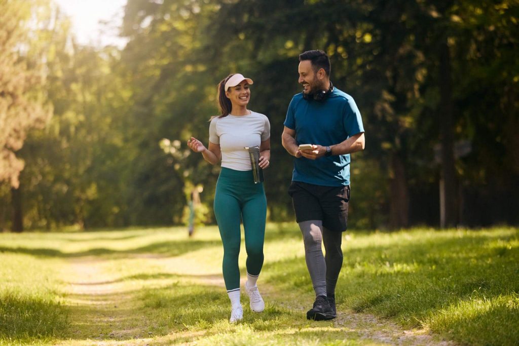 Happy couple enjoying a brisk walking cardio workout together in a green park
