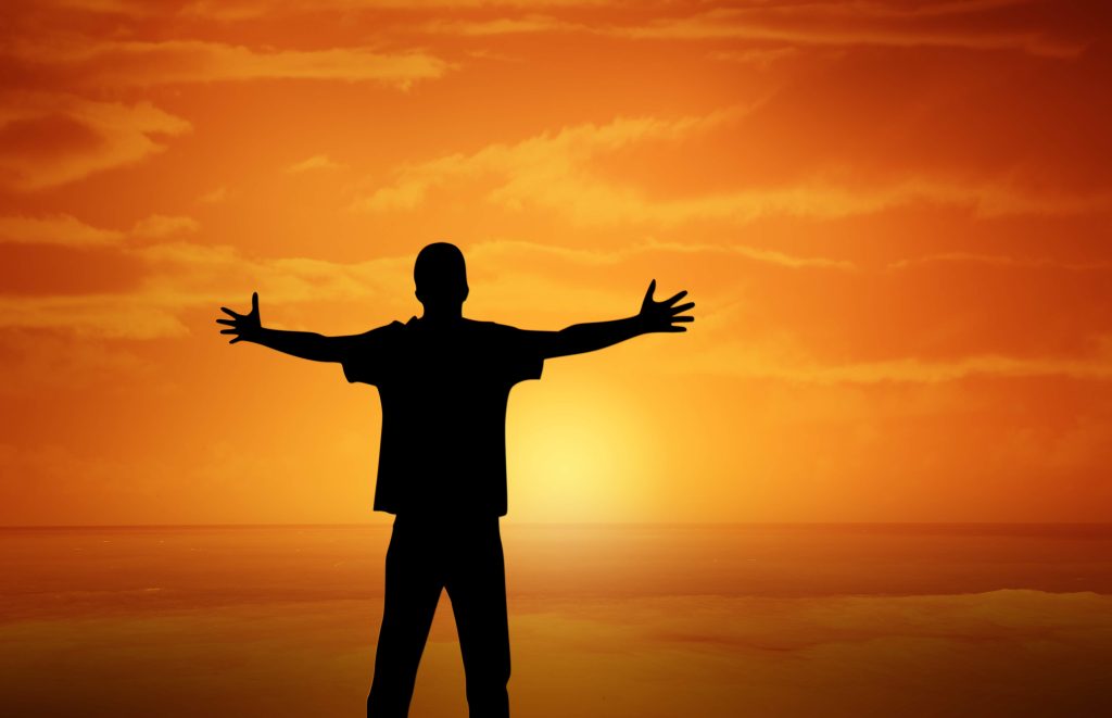 Man standing with open arms at sunrise tracking fitness goals and weight loss