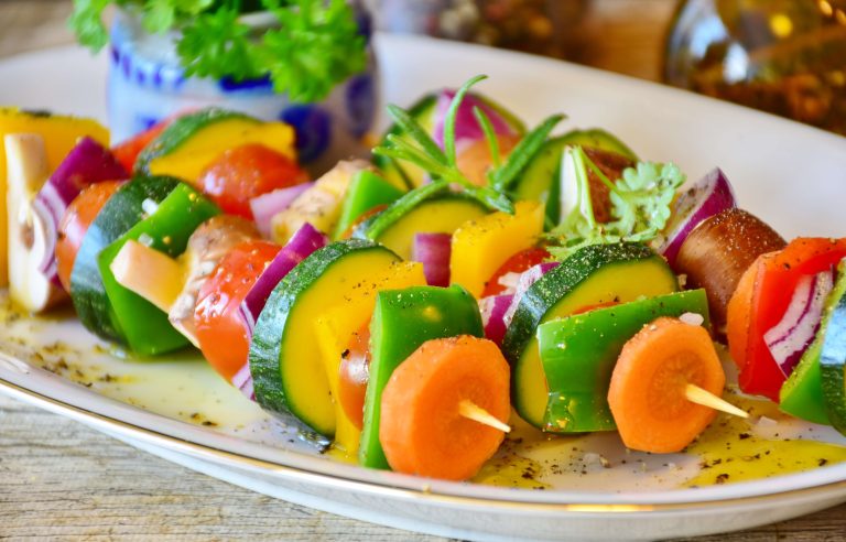 olorful fresh vegetable skewers with carrots, zucchini, onions, and tomatoes on a white platter, sprinkled with olive oil and spices, showing a healthy alternative to processed snacks