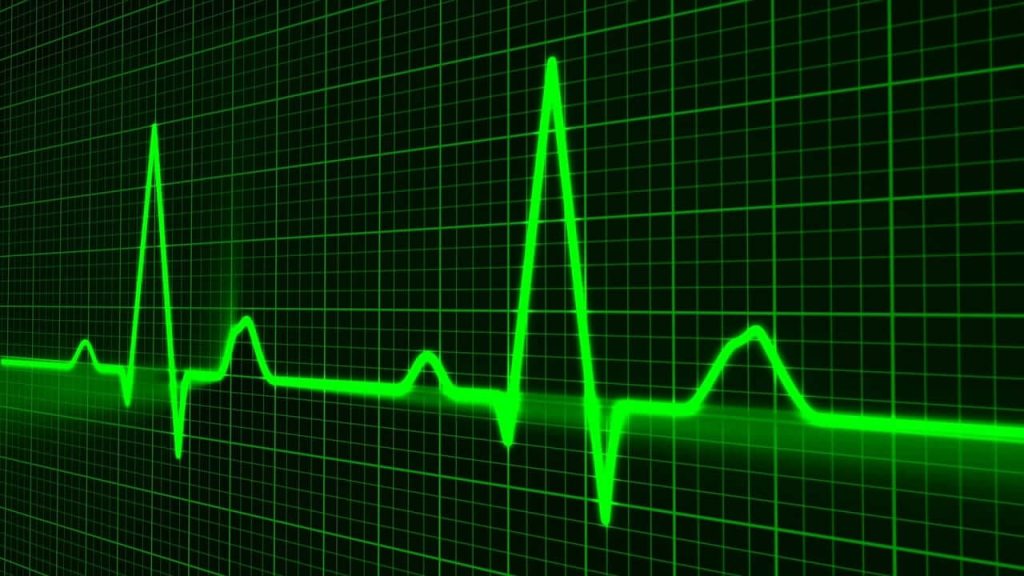 A glowing green heart rate monitor pulse trace on a dark grid background, illustrating how extreme heatwaves and climate conditions can place a silent strain on heart health.