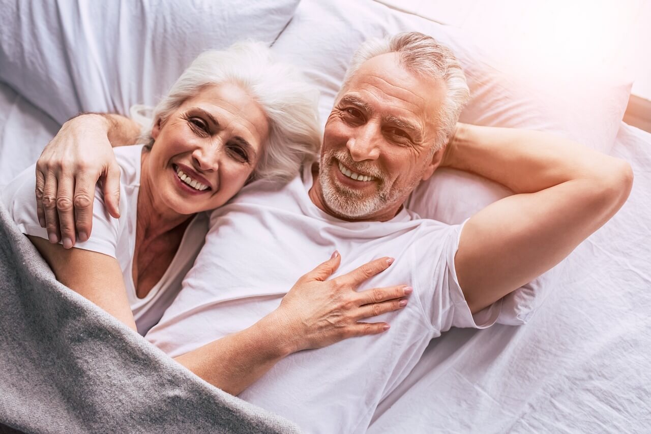 Smiling senior couple lying in bed and sharing a warm embrace showing intimacy and happiness