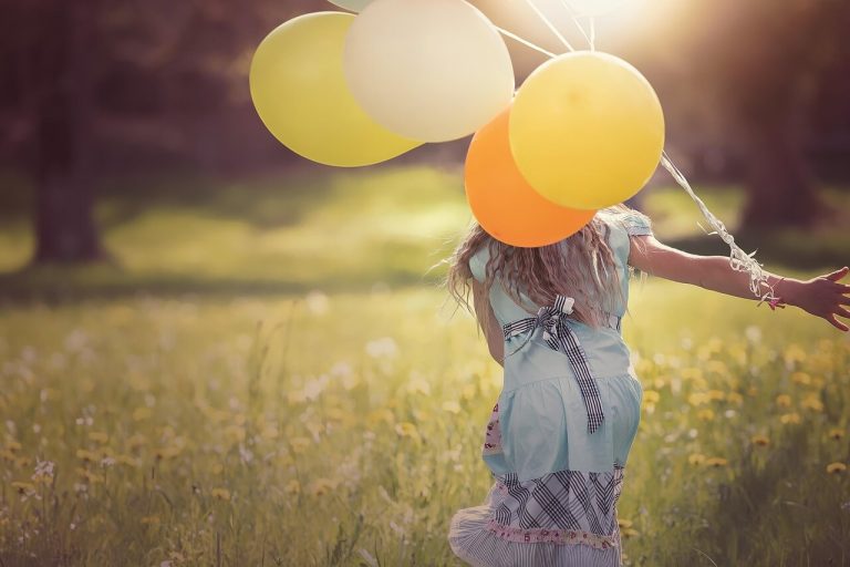 Little girl in a field holding balloons on a sunny day.