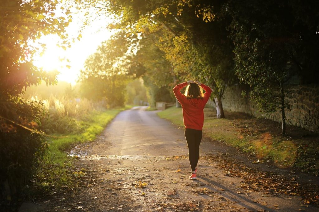 A person in a red hoodie walking on a tree-lined road during sunset for fitness.