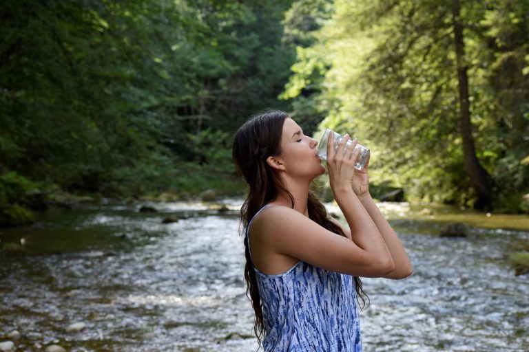 A young woman drinking a fresh glass of water in a beautiful forest nature background