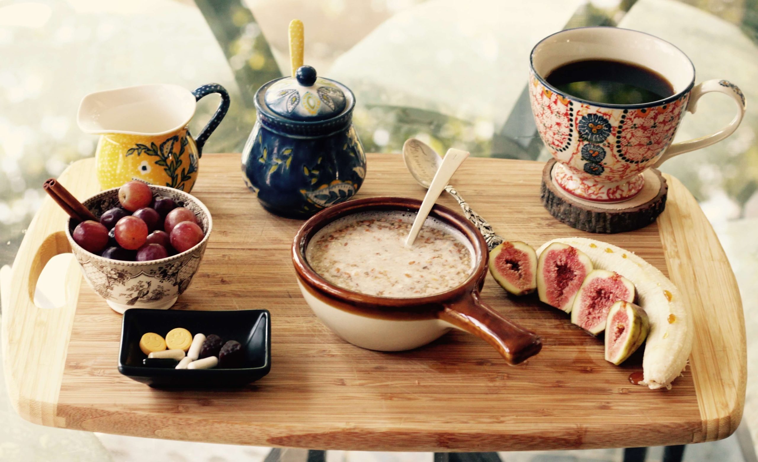 Healthy breakfast tray with oatmeal bowl, fresh grapes, sliced figs, banana, and coffee to boost workout energy