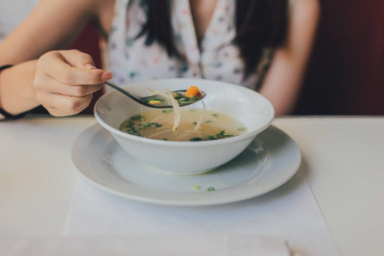 Woman eating a hot bowl of clear vegetable soup with a spoon to naturally reduce inflammation