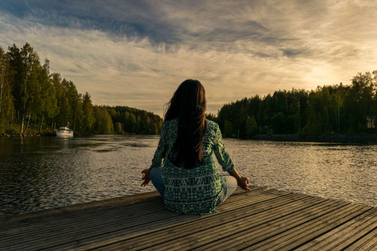 Woman meditating beside a river at sunset